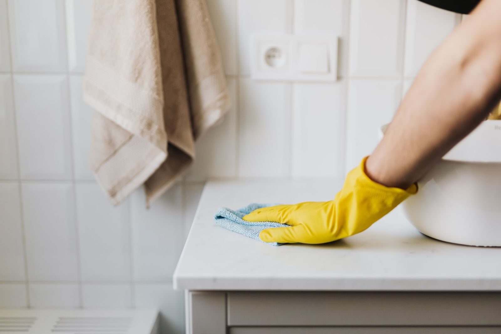 Hände in gelben Handschuhen reinigen den Schrank neben dem Waschbecken im Bad