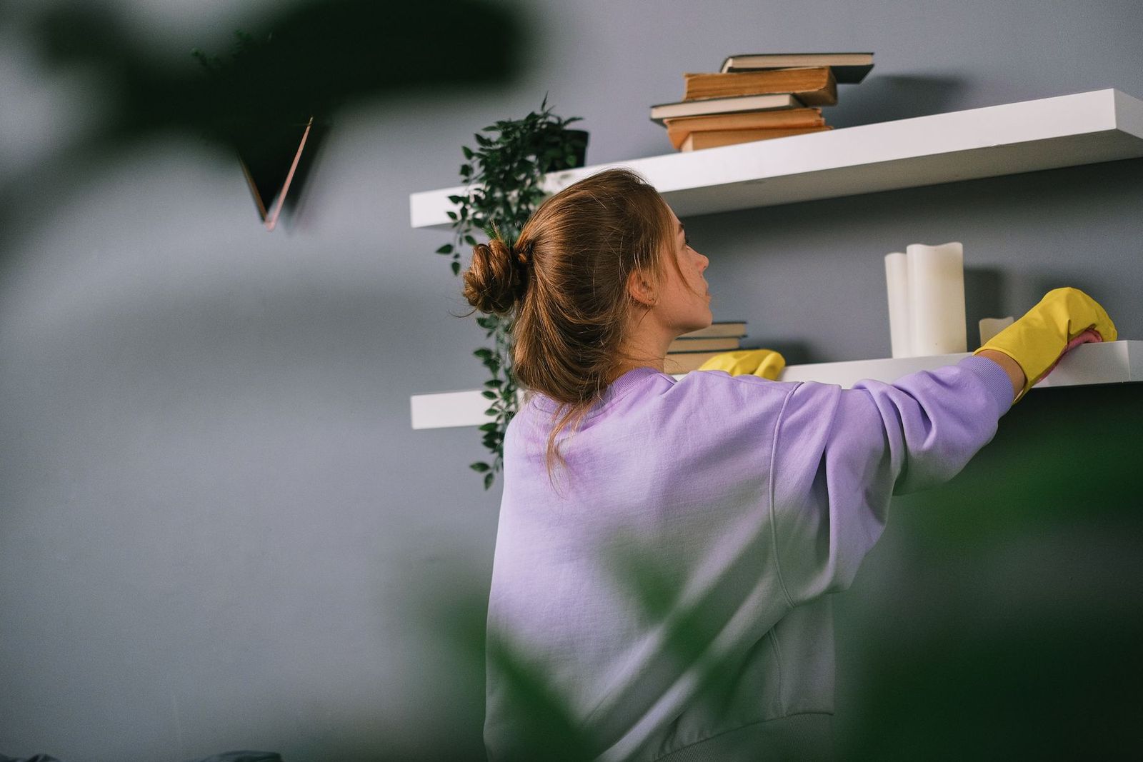 Junge Frau in gelben Handschuhen wischt ein Bücherregal ab